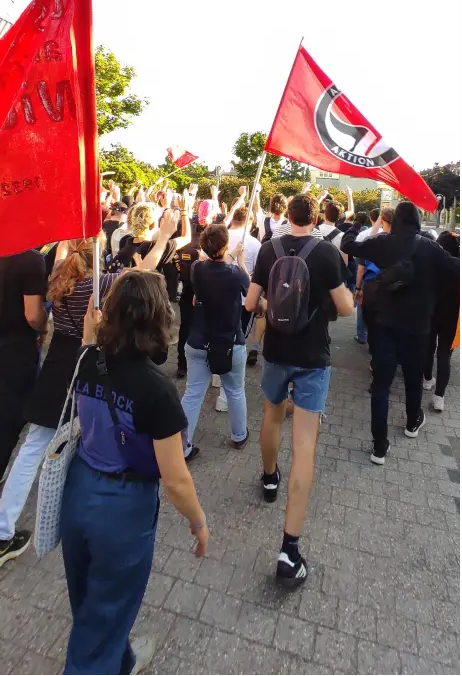 Das Bild zeigt einige Antifaschist:innen auf der Kundgebung mit einer Fahne der Antifaschistischen Aktion